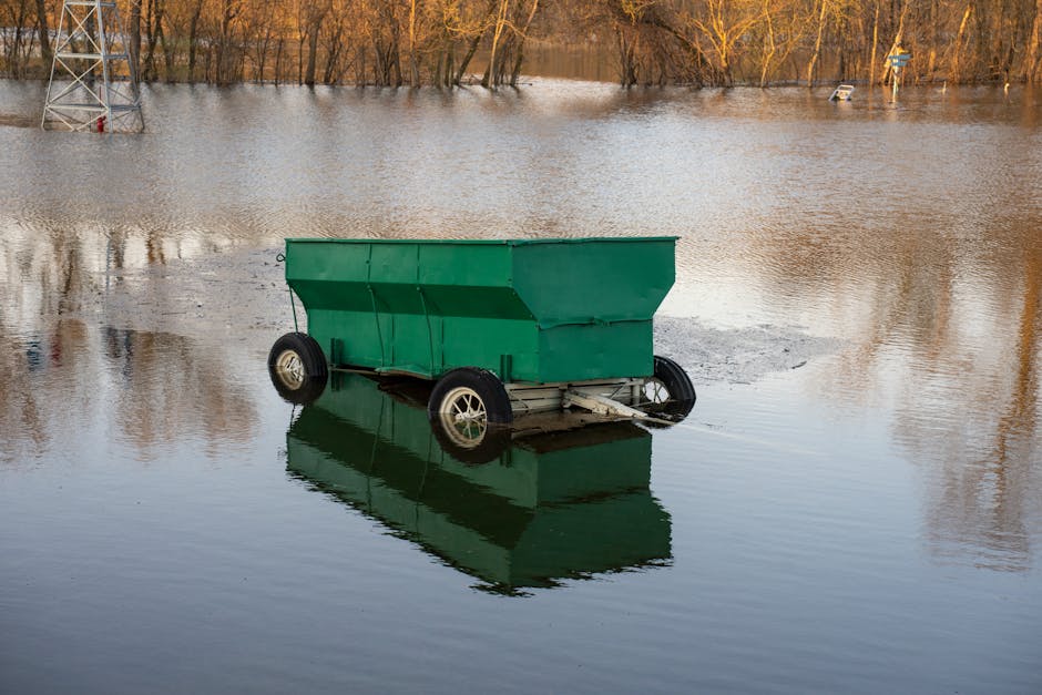 The image shows a flooded outdoor area with multiple wooden benches partially submerged in standing water. The benches, made of dark stained wood with slatted seats and backs, are arranged in a row al